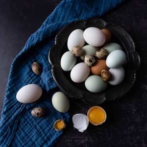 A variety of eggs on a pewter dish with a navy napkin and dark background